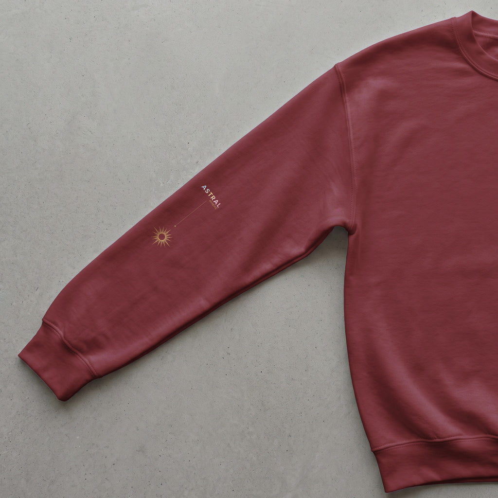 Maroon sweatshirt sleeve with golden sun graphic and "ASTRAL WHERE" text.