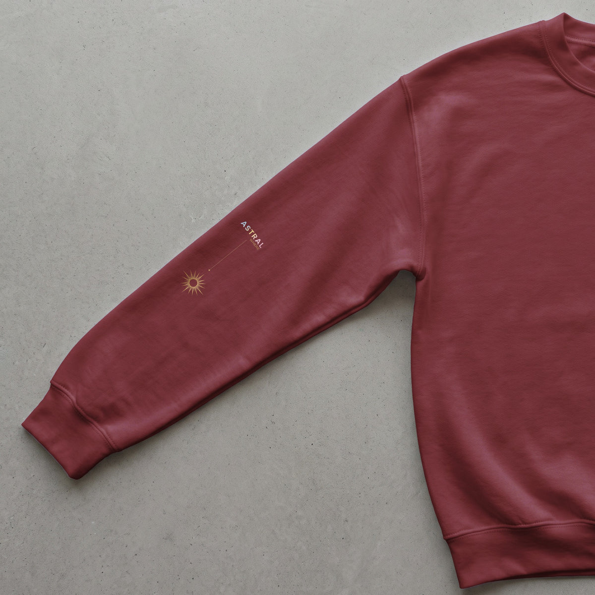 Maroon sweatshirt sleeve with golden sun graphic and "ASTRAL WHERE" text.