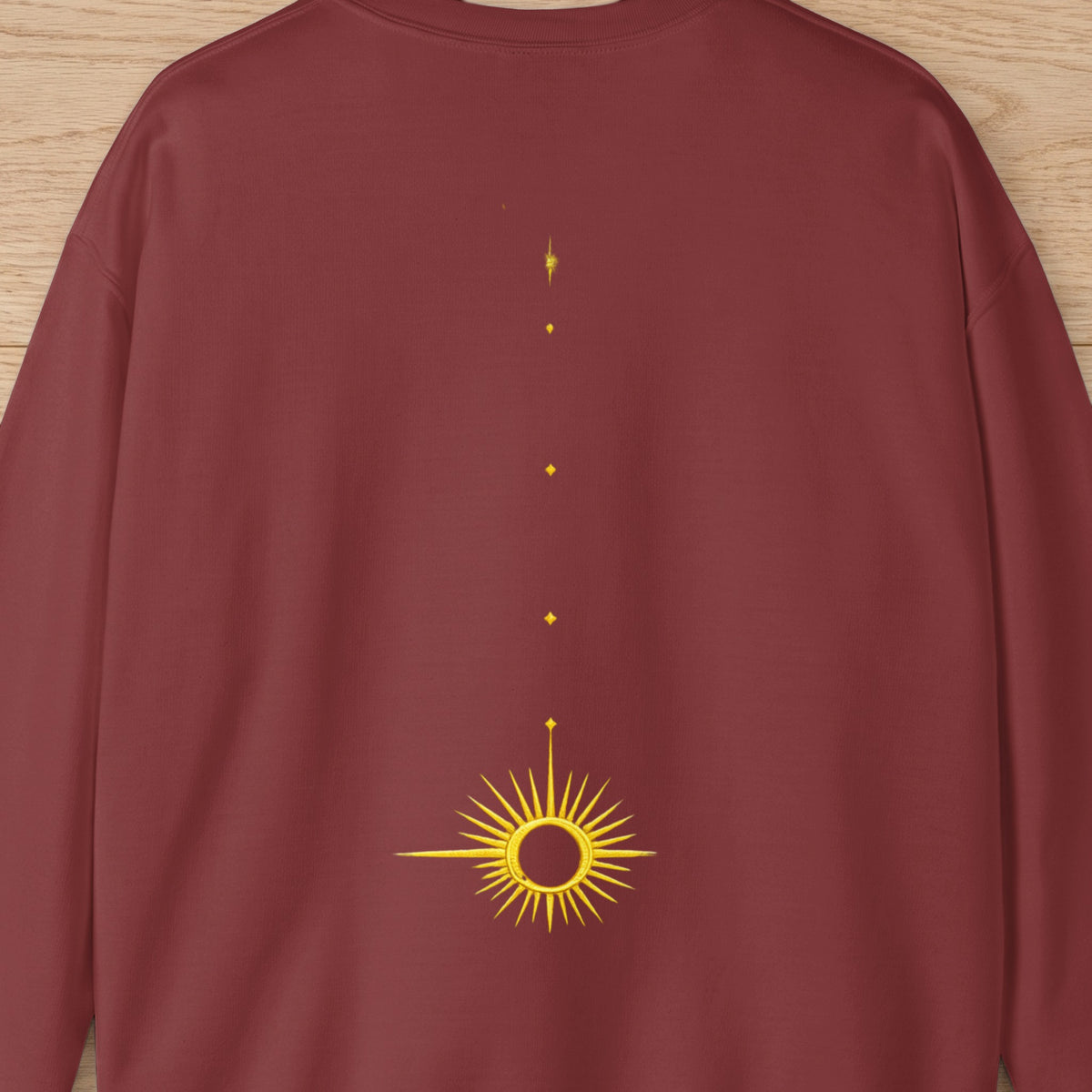 Maroon sweatshirt with embroidered gold sun and starburst design down the back.